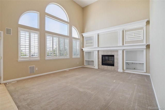 unfurnished living room with a high ceiling, light carpet, and a fireplace