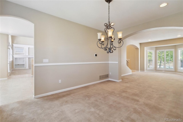 spare room featuring light colored carpet and an inviting chandelier