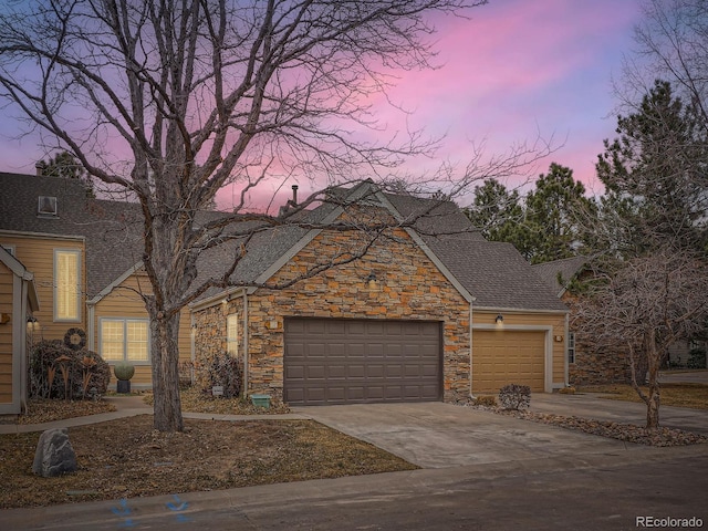 traditional home with a garage, stone siding, driveway, and a shingled roof