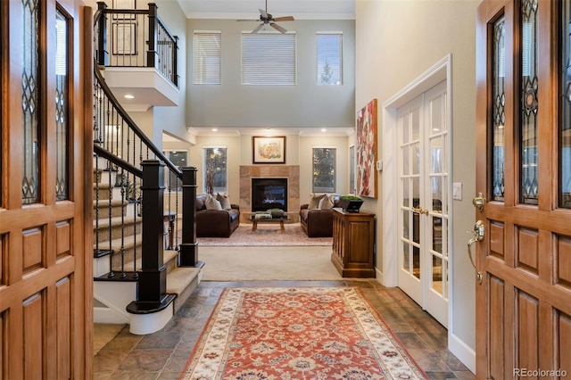 carpeted entryway with ceiling fan, a healthy amount of sunlight, crown molding, and a tile fireplace