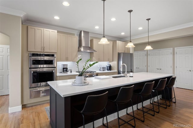 kitchen with light hardwood / wood-style flooring, wall chimney exhaust hood, stainless steel appliances, and a center island with sink