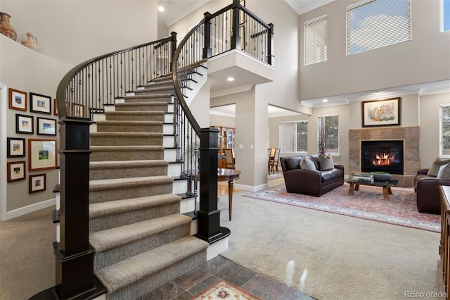 stairway with carpet floors, ornamental molding, a high ceiling, and a tiled fireplace