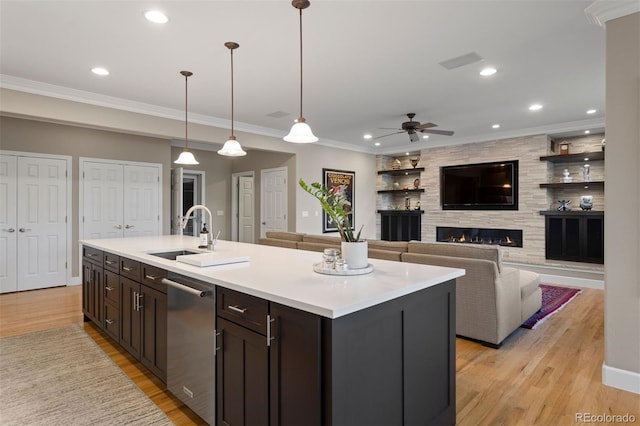 kitchen with pendant lighting, a center island with sink, sink, light wood-type flooring, and a large fireplace