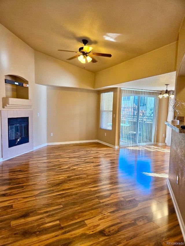 unfurnished living room with baseboards, a fireplace, a ceiling fan, and wood finished floors