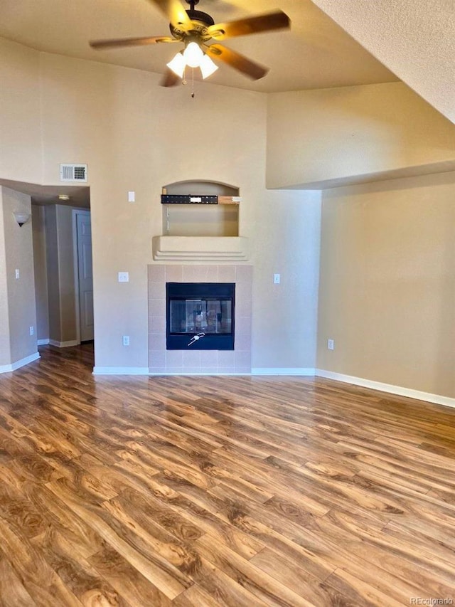 unfurnished living room with baseboards, visible vents, a ceiling fan, a tile fireplace, and wood finished floors