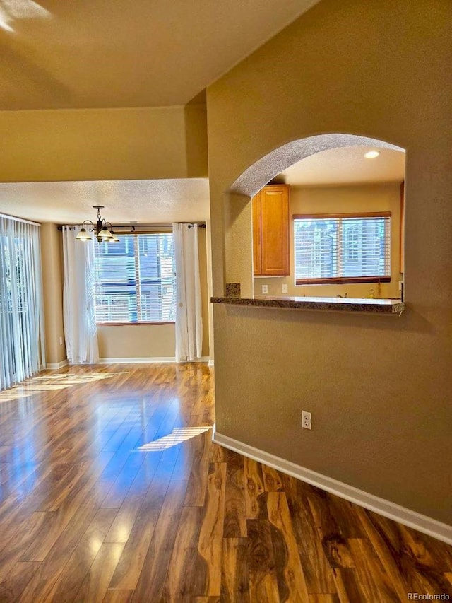 interior space featuring a notable chandelier, dark wood-style flooring, arched walkways, and baseboards