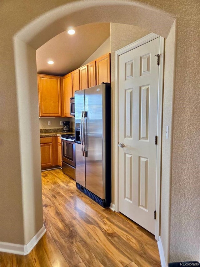 kitchen with arched walkways, appliances with stainless steel finishes, light wood-type flooring, and baseboards