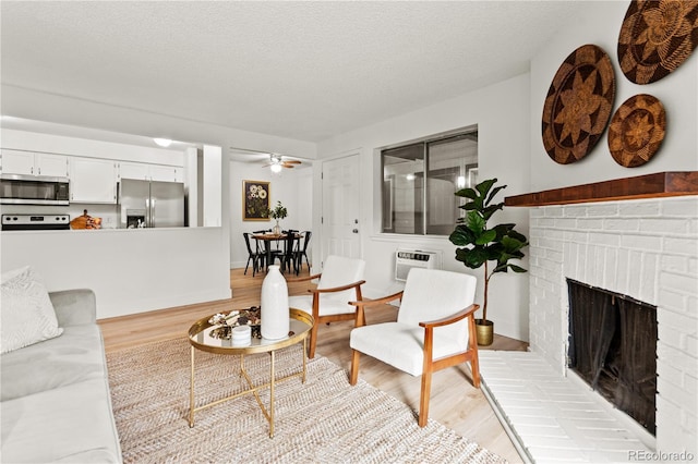 living room featuring ceiling fan, a wall mounted air conditioner, a fireplace, light hardwood / wood-style floors, and a textured ceiling