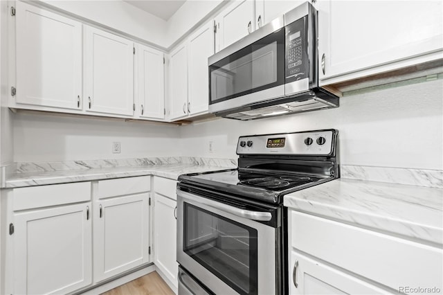 kitchen with white cabinetry, stainless steel appliances, light stone countertops, and light wood-type flooring