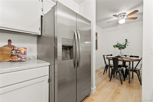 kitchen featuring light hardwood / wood-style flooring, a textured ceiling, stainless steel fridge, light stone countertops, and white cabinets