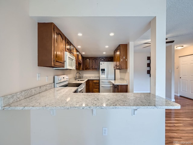 kitchen with ceiling fan, dark hardwood / wood-style floors, kitchen peninsula, white appliances, and a kitchen bar