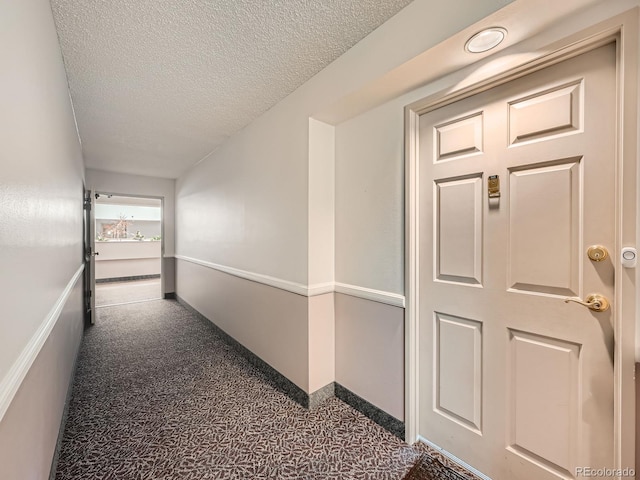 hall with dark colored carpet and a textured ceiling