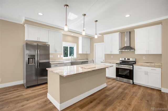 kitchen featuring appliances with stainless steel finishes, hanging light fixtures, a kitchen island, hardwood / wood-style flooring, and wall chimney range hood