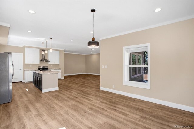 kitchen with hanging light fixtures, wall chimney exhaust hood, white cabinetry, stainless steel appliances, and light hardwood / wood-style floors