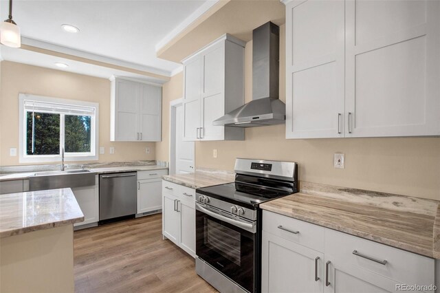 kitchen featuring appliances with stainless steel finishes, white cabinets, pendant lighting, light hardwood / wood-style flooring, and wall chimney range hood