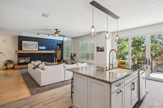 kitchen with a sink, light wood-type flooring, a glass covered fireplace, and ceiling fan