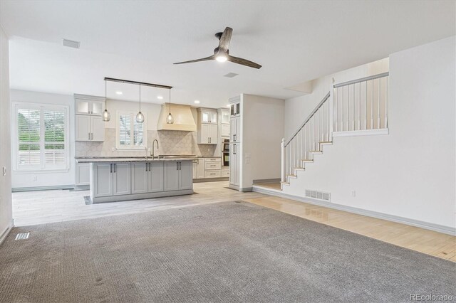unfurnished living room featuring ceiling fan, baseboards, light wood-style flooring, a sink, and stairway