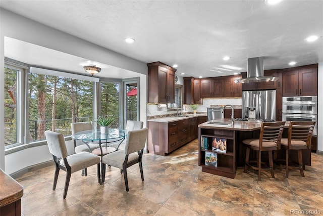 kitchen featuring sink, tasteful backsplash, island range hood, stainless steel appliances, and a kitchen island with sink