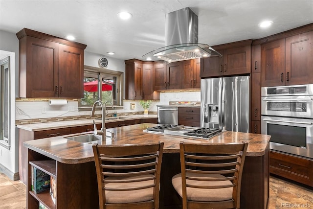 kitchen featuring sink, a breakfast bar area, appliances with stainless steel finishes, an island with sink, and island exhaust hood