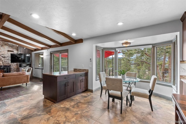 kitchen featuring dark brown cabinetry, vaulted ceiling with beams, a fireplace, and a textured ceiling