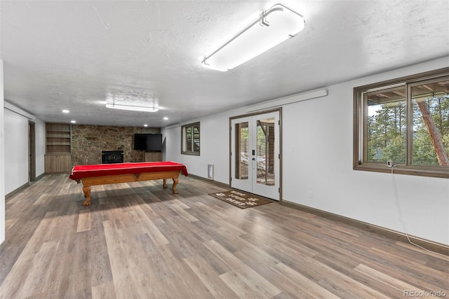 rec room featuring hardwood / wood-style flooring, billiards, a fireplace, a textured ceiling, and french doors