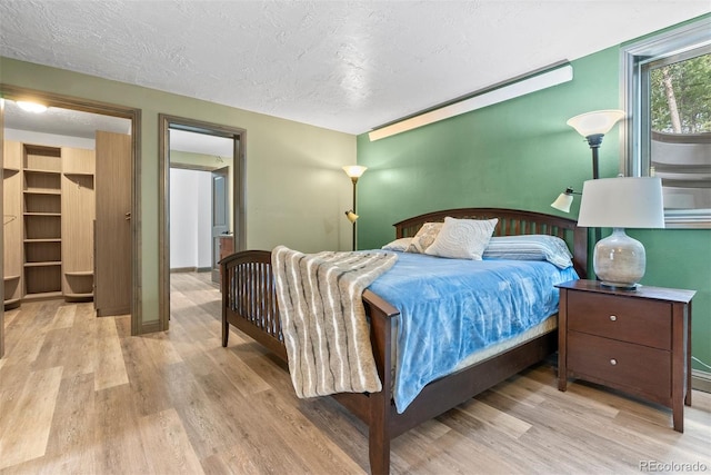 bedroom with a walk in closet, light hardwood / wood-style flooring, and a textured ceiling