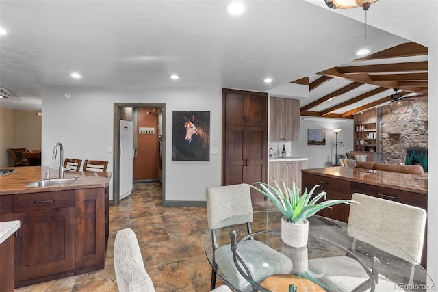 dining area featuring vaulted ceiling with beams, sink, a stone fireplace, ceiling fan, and built in features