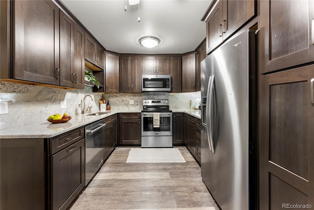 kitchen featuring sink, stainless steel appliances, light stone counters, and dark brown cabinetry