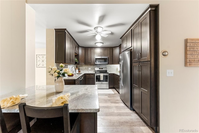 kitchen with light stone counters, light hardwood / wood-style flooring, kitchen peninsula, dark brown cabinets, and appliances with stainless steel finishes