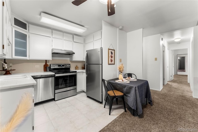 kitchen with tile counters, appliances with stainless steel finishes, ceiling fan, sink, and white cabinetry