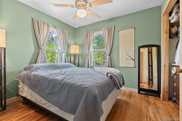 bedroom with wood finished floors, multiple windows, baseboards, and ceiling fan