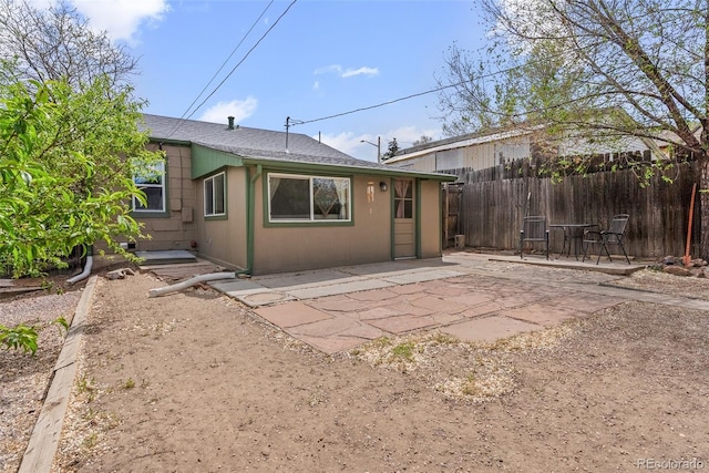rear view of property with fence, a patio, and a shingled roof