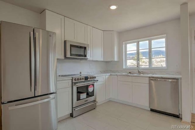 kitchen with light stone counters, appliances with stainless steel finishes, sink, and white cabinets