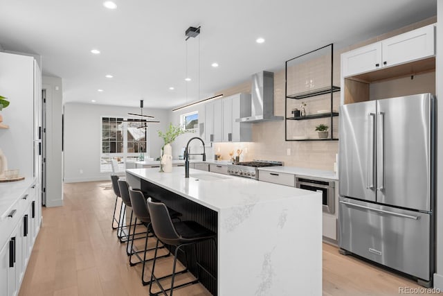 kitchen with stainless steel appliances, wall chimney range hood, open shelves, and hanging light fixtures