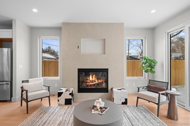 living area featuring light wood-type flooring, a tile fireplace, a healthy amount of sunlight, and recessed lighting