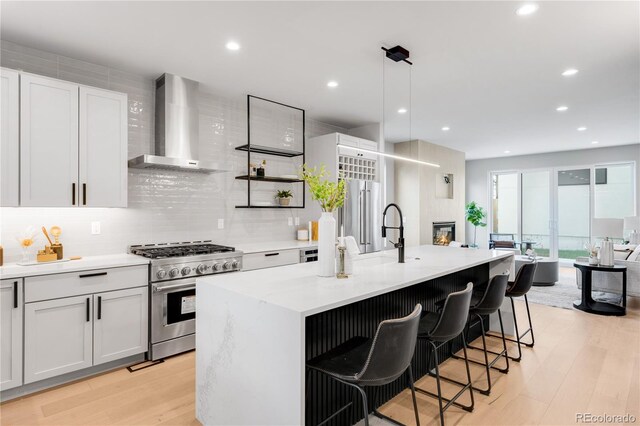 2520 S Cherokee St, Denver, CO 80223 - kitchen featuring high end stove, light wood finished floors, wall chimney range hood, tasteful backsplash, and an island with sink