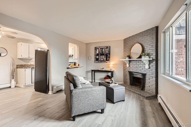 living room with baseboard heating, ceiling fan, a fireplace, and light hardwood / wood-style flooring