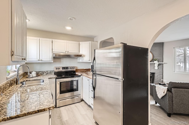 kitchen with sink, dark stone countertops, light hardwood / wood-style floors, white cabinets, and appliances with stainless steel finishes