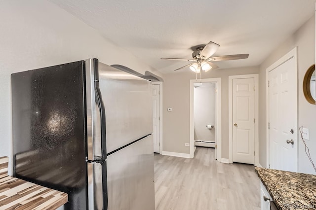 kitchen featuring dark stone counters, ceiling fan, a baseboard radiator, light hardwood / wood-style flooring, and stainless steel refrigerator