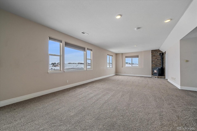 unfurnished living room with vaulted ceiling, light colored carpet, a textured ceiling, and a wood stove