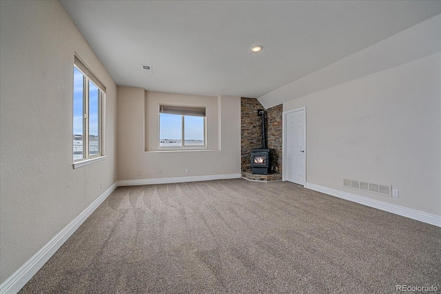 unfurnished living room with carpet floors, lofted ceiling, and a wood stove