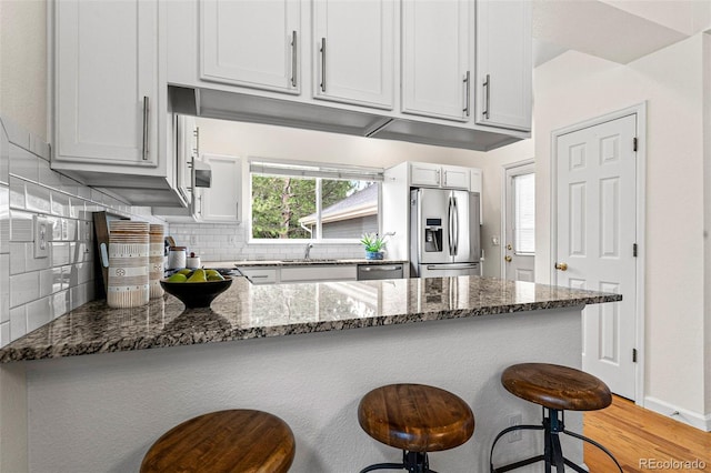 kitchen featuring decorative backsplash, stainless steel appliances, light hardwood / wood-style flooring, and dark stone countertops