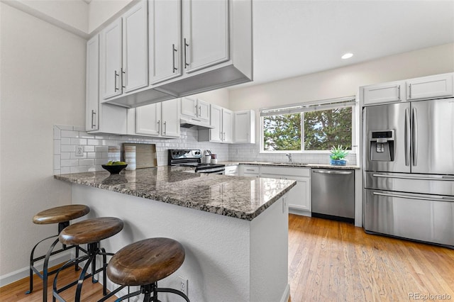 kitchen featuring stainless steel appliances, light hardwood / wood-style floors, white cabinetry, and dark stone counters