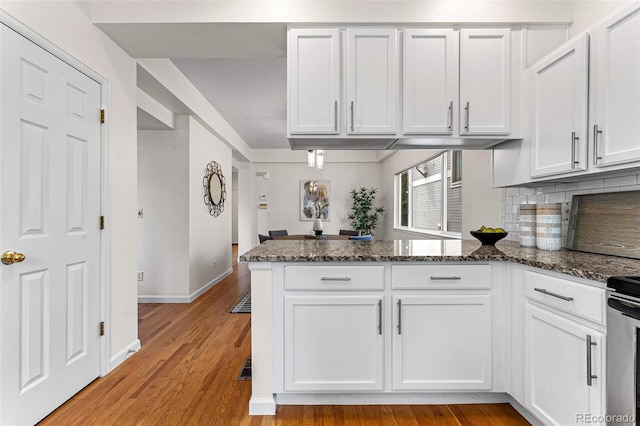 kitchen with light wood-type flooring, white cabinetry, and dark stone counters