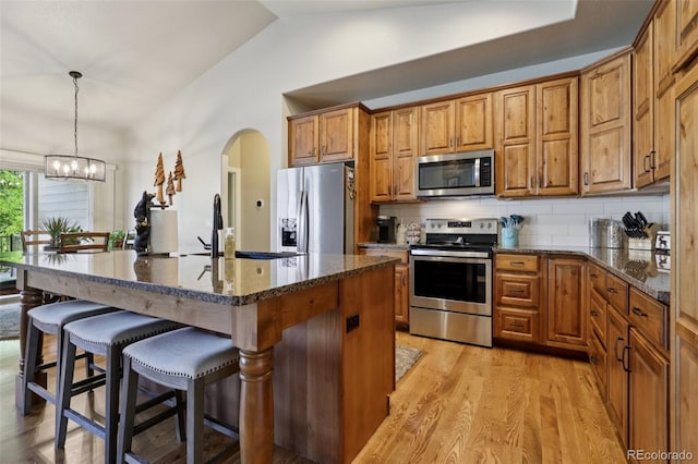 3125 Brunner Blvd, Johnstown, CO 80534 - kitchen with stainless steel appliances, vaulted ceiling, arched walkways, a kitchen breakfast bar, and brown cabinets