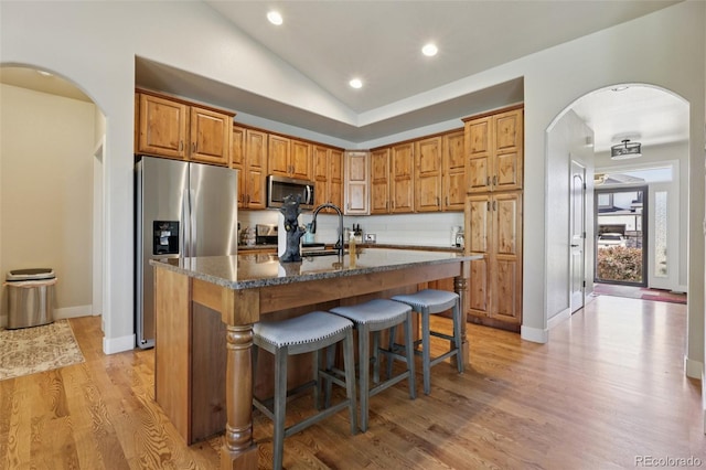 3125 Brunner Blvd, Johnstown, CO 80534 - kitchen with appliances with stainless steel finishes, arched walkways, vaulted ceiling, light wood finished floors, and a breakfast bar