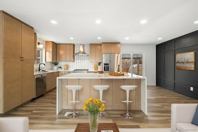 kitchen with wall chimney exhaust hood, sink, a center island, appliances with stainless steel finishes, and backsplash