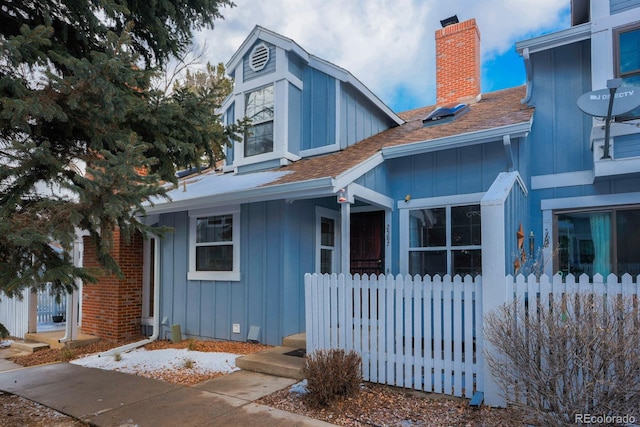 view of front of home with roof with shingles, board and batten siding, a chimney, and fence