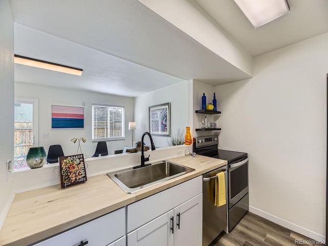 kitchen with white cabinets, baseboards, a sink, dark wood-style flooring, and appliances with stainless steel finishes
