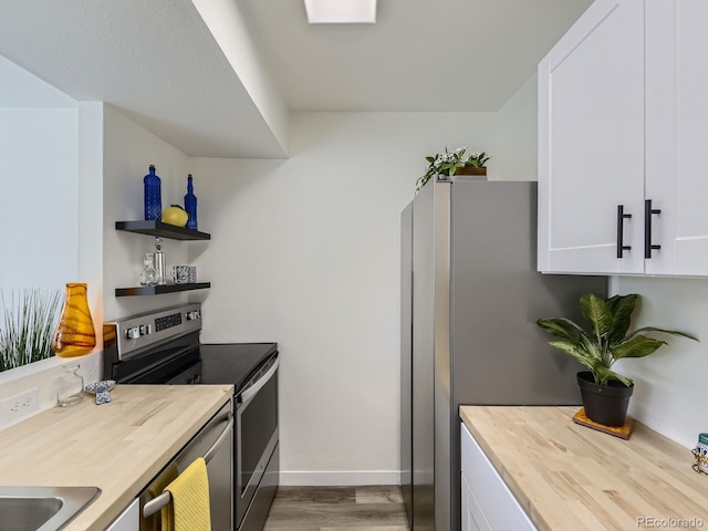 kitchen with baseboards, wood counters, white cabinetry, appliances with stainless steel finishes, and wood finished floors